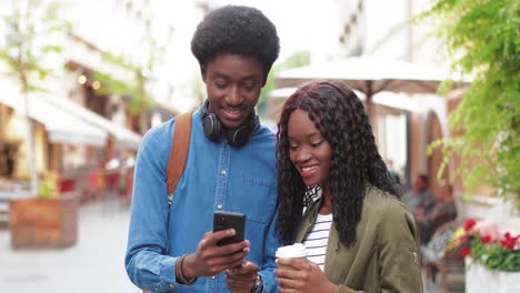 African-american-man-and-woman-watching-something-in-a-smartphone-in-the-street