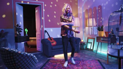 Young-stylish-caucasian-man-with-long-hair-holding-empty-frame-and-dancing-energetically-in-a-retro-party-at-home