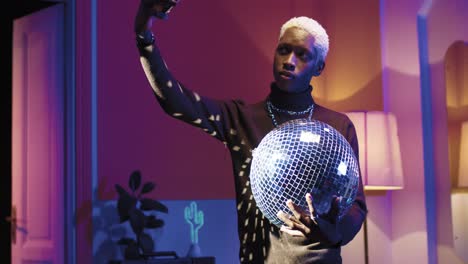 Young-stylish-african-american-holding-disco-ball-and-making-selfies-using-smartphone-in-a-retro-party-at-home