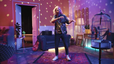 Young-stylish-caucasian-man-with-long-hair-in-glasses-dancing-energetically-in-a-retro-party-at-home