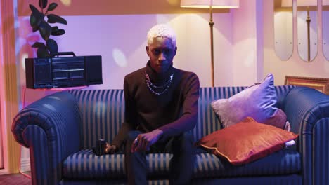 African-american-man-with-blonde-hair-taking-pictures-to-the-camera-while-sitting-on-sofa-in-a-retro-room-at-home