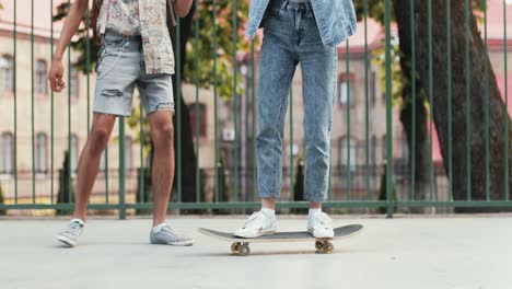 Full-length-view-of-a-teenage-girl-riding-a-skateboard-while-her-african-american-boyfriend-helping-her-maintain-balance-in-the-street