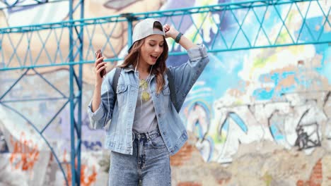 Caucasian-girl-wearing-cap-and-headphones-listening-to-the-music-on-the-smartphone-while-dancing-in-the-street