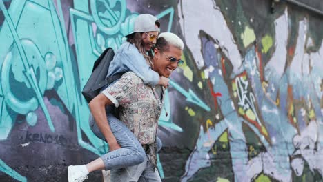 Young-boy-giving-her-girlfriend-a-piggyback-near-a-graffity-wall-in-the-street