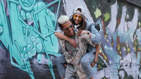 Young-boy-giving-her-girlfriend-a-piggyback-near-a-graffity-wall-in-the-street