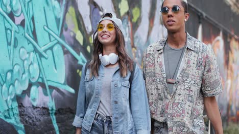 Hipster-couple-in-stylish-clothes-in-love-talking-and-walking-down-the-street-near-a-graffity-wall