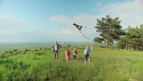 Caucasian-senior-man-running-with-his-grandchildren-in-the-park-while-they-are-flying-a-kite-on-a-sunny-day
