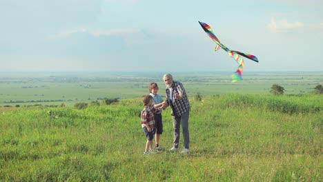 Caucasian-senior-man-with-his-grandchildren-in-the-park-while-they-are-flying-a-kite-on-a-sunny-day