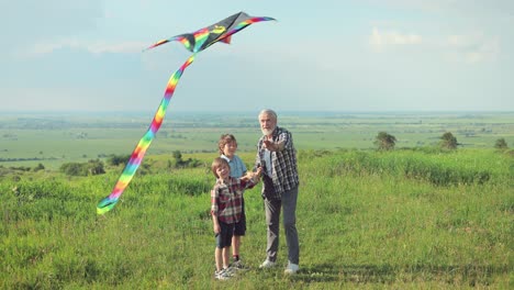 Caucasian-senior-man-with-his-grandchildren-in-the-park-while-they-are-flying-a-kite-on-a-sunny-day