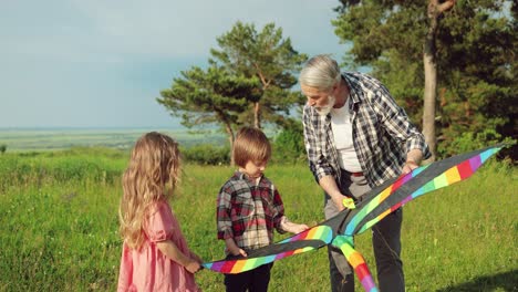 Happy-and-joyful-caucasian-sister-and-brother,-playing-with-their-grandfather-with-a-kite-and-looking-at-camera