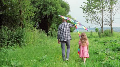 Rear-view-of-caucasian-senior-man-and-his-little-granddaughter-playing-with-a-kite-in-the-park-on-a-sunny-day