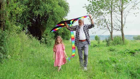 Front-view-of-caucasian-senior-man-and-his-little-granddaughter-playing-with-a-kite-in-the-park-on-a-sunny-day