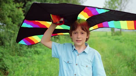 Close-up-view-of-a-little-boy-holding-a-kite-and-looking-at-the-camera-in-the-park-on-a-sunny-day