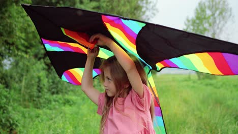 Close-up-view-of-a-little-girl-holding-a-kite-and-looking-at-the-camera-in-the-park-on-a-sunny-day