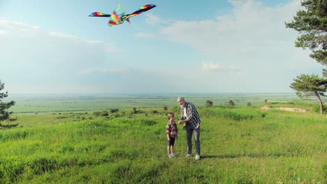 Distant-view-of-caucasian-senior-man-and-his-grandson-in-the-park-while-they-are-flying-a-kite-on-a-sunny-day