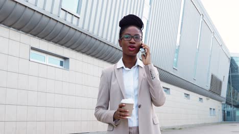 Afroamerikanische-Geschäftsfrau-In-Stilvoller-Kleidung-Und-Brille,-Die-Auf-Dem-Smartphone-Spricht-Und-Kaffee-Hält,-Um-Auf-Die-Straße-Zu-Gehen