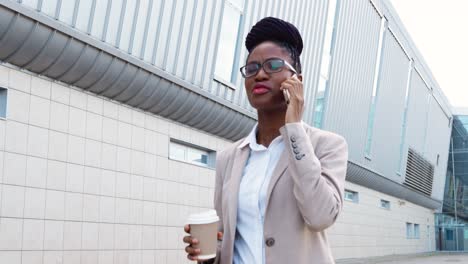 Mujer-De-Negocios-Afroamericana-Con-Ropa-Y-Gafas-Elegantes-Hablando-Por-Teléfono-Inteligente-Y-Tomando-Café-Para-Ir-A-La-Calle