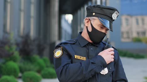 Kaukasischer-Polizist-Mit-Schutzmaske-Und-Kappe,-Der-Auf-Der-Straße-Im-Radio-Spricht