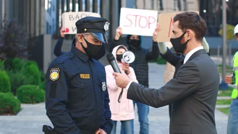 Kaukasischer-Journalist-Oder-Korrespondent-Mit-Schutzmaske-In-Einem-Interview-Mit-Einem-Polizisten-Aus-Protest-Gegen-Covid-19