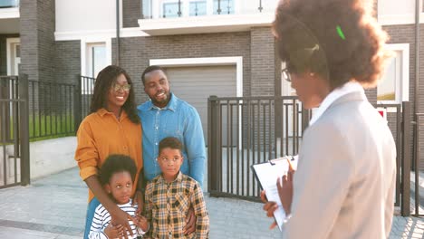 Feliz-Familia-Afroamericana-Con-Dos-Niños-Pequeños-Comprando-Una-Casa-En-Los-Suburbios-Y-Hablando-Con-Una-Agente-Inmobiliaria-Al-Aire-Libre
