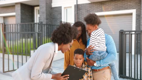 Cheerful-African-American-family-with-small-kids-buying-house-at-suburbs-and-talking-with-female-real-estate-agent-outside