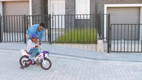 Happy-African-American-father-teaching-small-pretty-girl-in-helmet-riding-on-bike-at-street-in-outskirt