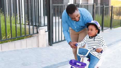 African-American-father-teaching-small-girl-in-helmet-riding-on-bike-at-street-in-outskirt