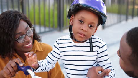 Close-up-of-small-African-American-cute-girl-in-helmet-sitting-on-bike-and-listening-to-her-smiled-parents