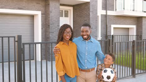 Portrait-of-happy-African-American-family-with-small-cute-boy-standing-at-street-near-house-at-suburb-and-smiling-to-camera