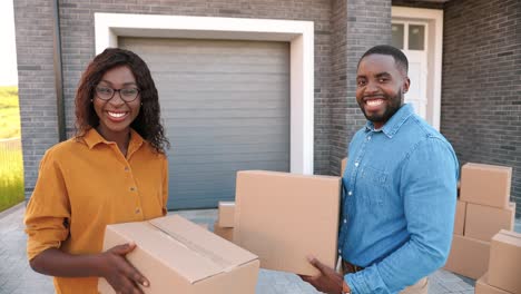 Rear-view-on-African-American-young-couple-walking-in-yard-at-big-house-and-carrying-carton-boxes