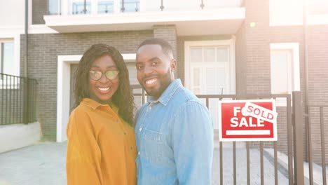 Portrait-of-happy-African-American-married-couple-standing-at-new-house-at-suburb-and-smiling-cheerfully