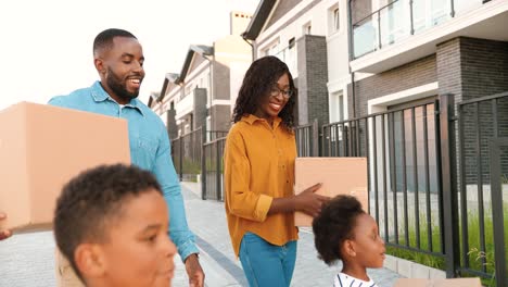 Happy-African-American-parents-with-children-moving-in-new-home-and-carrying-carton-boxes