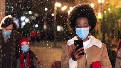 Porträt-Einer-Afroamerikanischen-Frau,-Die-Auf-Der-Straße-Auf-Dem-Smartphone-Tippt,-Während-Es-Zu-Weihnachten-Schneit