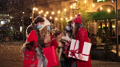 Fröhliche-Multiethnische-Freunde-Reden-Und-Halten-Geschenke-Auf-Der-Straße,-Während-Es-Zu-Weihnachten-Schneit