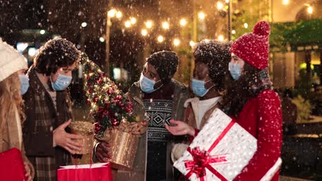 Happy-multiethnic-friends-talking-and-holding-presents-on-the-street-while-it¬¥s-snowing-in-Christmas