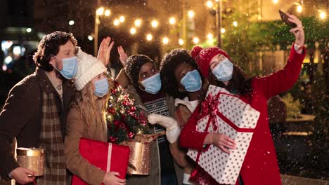 Retrato-De-Felices-Amigos-Multiétnicos-Haciéndose-Un-Selfie-Y-Sosteniendo-Regalos-En-La-Calle-Mientras-Nieva-En-Navidad