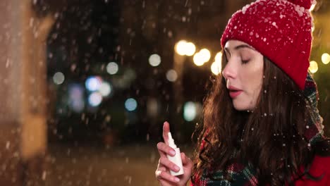 Close-up-view-of-sick-Caucasian-woman-in-red-coat-outdoor-using-nose-spray-on-the-street-while-it¬¥s-snowing-in-Christmas
