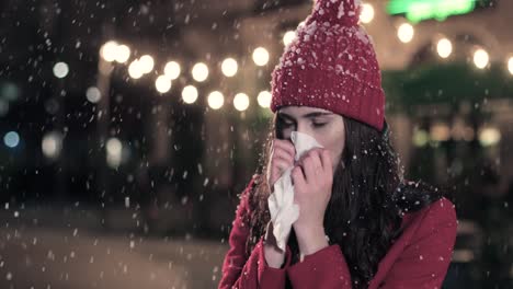 Close-up-view-of-sick-Caucasian-woman-in-red-coat-blowing-her-nose-on-the-street-while-it¬¥s-snowing-in-Christmas