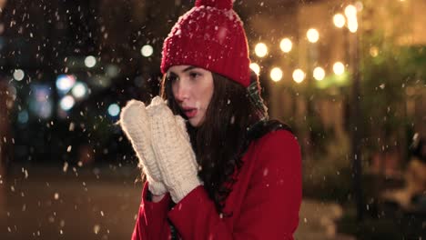 Nahaufnahme-Einer-Kaukasischen-Frau-In-Rotem-Mantel-Und-Handschuhen,-Die-Sich-Auf-Der-Straße-Die-Hände-Wärmt,-Während-Es-Zu-Weihnachten-Schneit