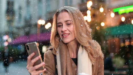 Nahaufnahme-Einer-Kaukasischen-Frau-Mit-Smartphone-Auf-Der-Straße,-Während-Es-Zu-Weihnachten-Schneit