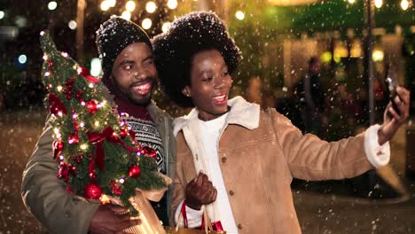 Vista-De-Cerca-De-Una-Alegre-Pareja-Afroamericana-Haciéndose-Un-Selfie-Con-Un-Smartphone-Mientras-Nieva-En-La-Calle-En-Navidad
