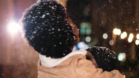 Nahaufnahme-Eines-Fröhlichen-Afroamerikanischen-Paares,-Das-Sich-Umarmt-Und-Lächelt,-Während-Es-Zu-Weihnachten-Auf-Der-Straße-Schneit