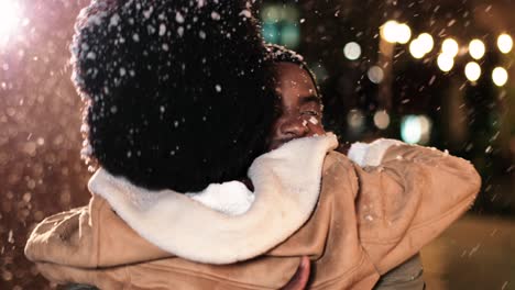 Nahaufnahme-Eines-Fröhlichen-Afroamerikanischen-Paares,-Das-Sich-Umarmt-Und-Lächelt,-Während-Es-Zu-Weihnachten-Auf-Der-Straße-Schneit