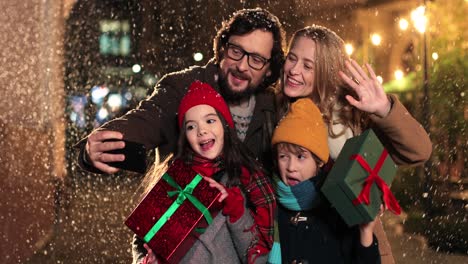 Vista-De-Cerca-De-Una-Familia-Feliz-Caucásica-Sosteniendo-Regalos-Y-Haciéndose-Un-Selfie-Mientras-Nieva-En-Navidad