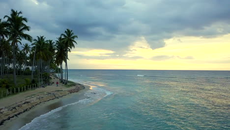 Flying-over-an-exotic-beach-with-palm-trees-at-sunset