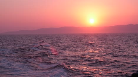 Beautiful-pink-sunset-over-the-Mediterranean-sea-as-waves-crash-with-mountains-in-the-background