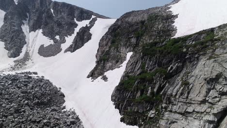 Aerial-of-snow-covered-peak,-close-to-cliff-to-show-small-waterfalls-and-small-ice-cave