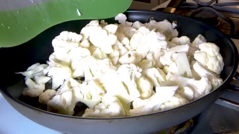 Adding-raw-cauliflower-to-a-frying-pan,-CLOSE-UP