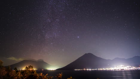 Stars-rotating-over-a-bright-city,-volcanoes,-and-Lake-Atitlan-in-Ecuador,-TIMELAPSE