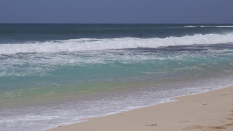 Rolling-Ocean-Waves-Crashing-Onto-Sandy-Beach-Past-Surfers-in-Hawaii